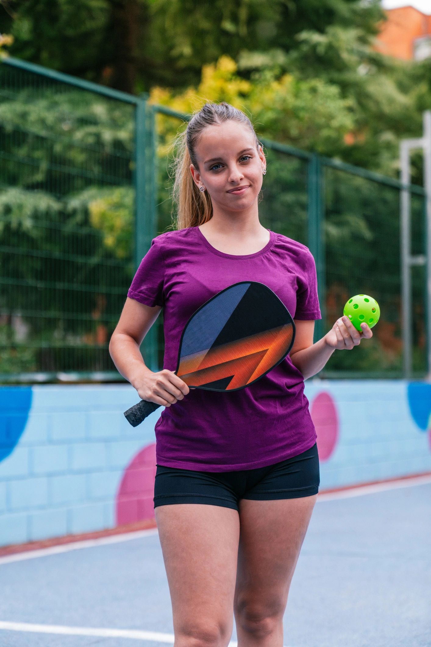 Woman holding a pickleball paddle and ball on court